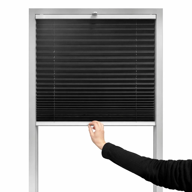 Cu mâna se mișcă roleta plisse de sus în jos pentru reglarea umbririi la fereastră.