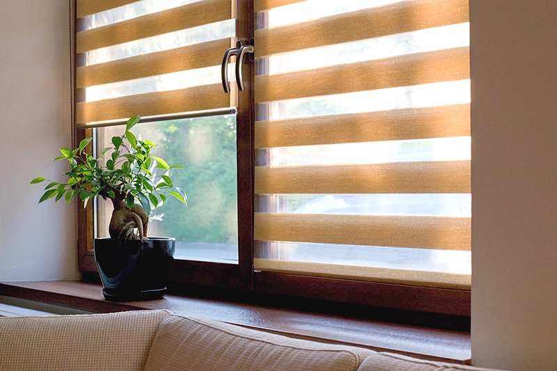 Roletă modernă fixată pe o fereastră din lemn, atenuează lumina puternică a soarelui din exterior