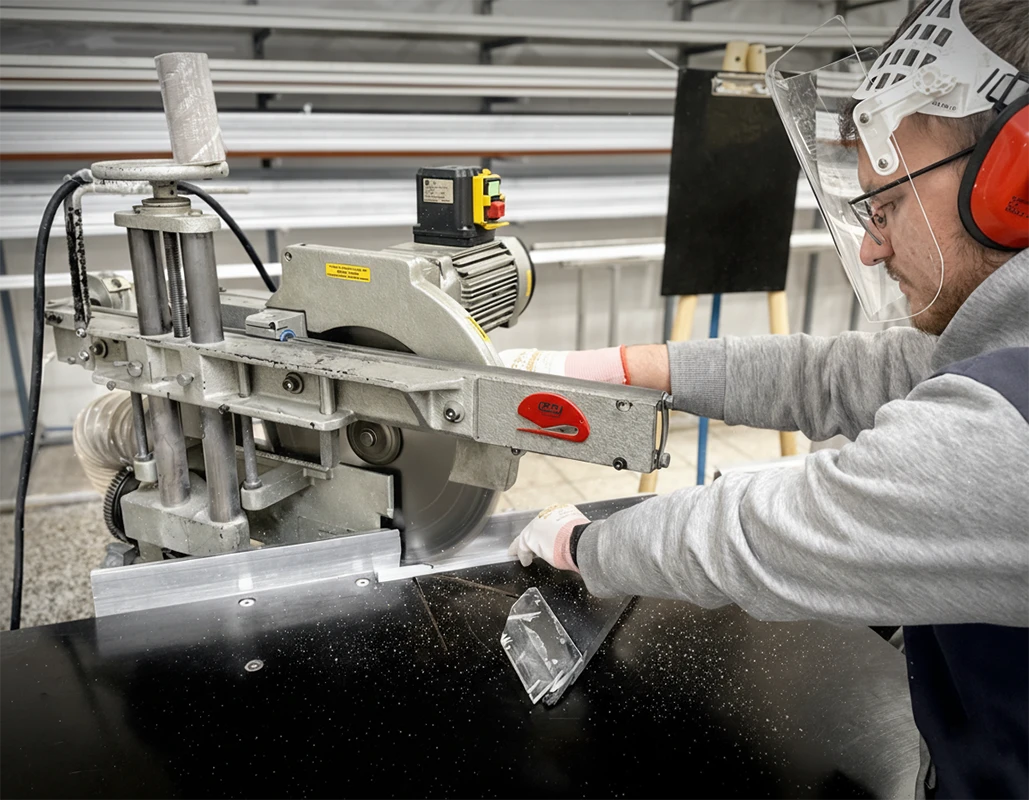 Lucrător taie materialul pentru fabricarea plaselor anti-insecte alături de prezentarea tipurilor de plasă – gri, neagră și PET rezistentă